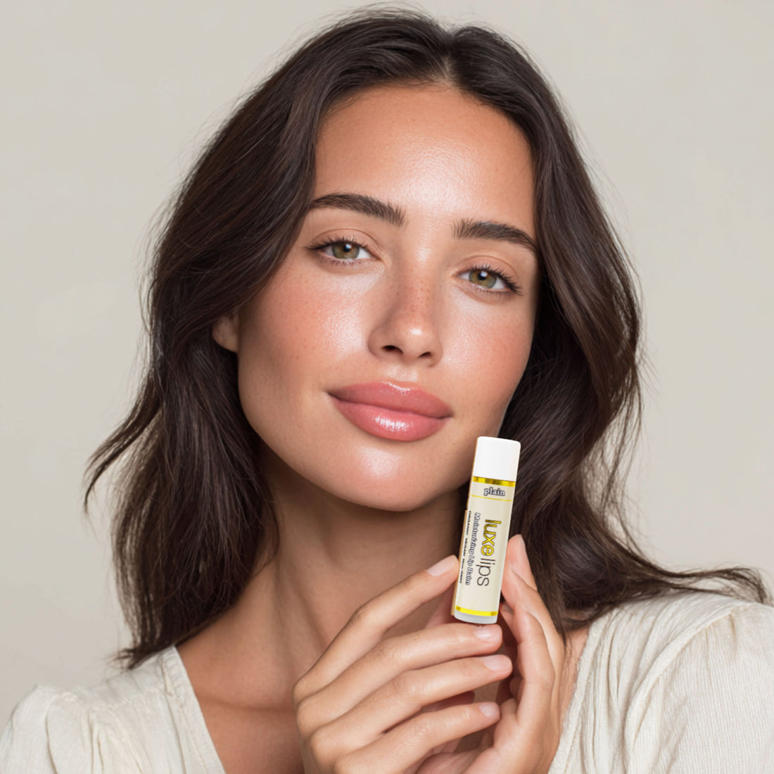 Woman holding a Luxe Lipslip balm with a neutral background