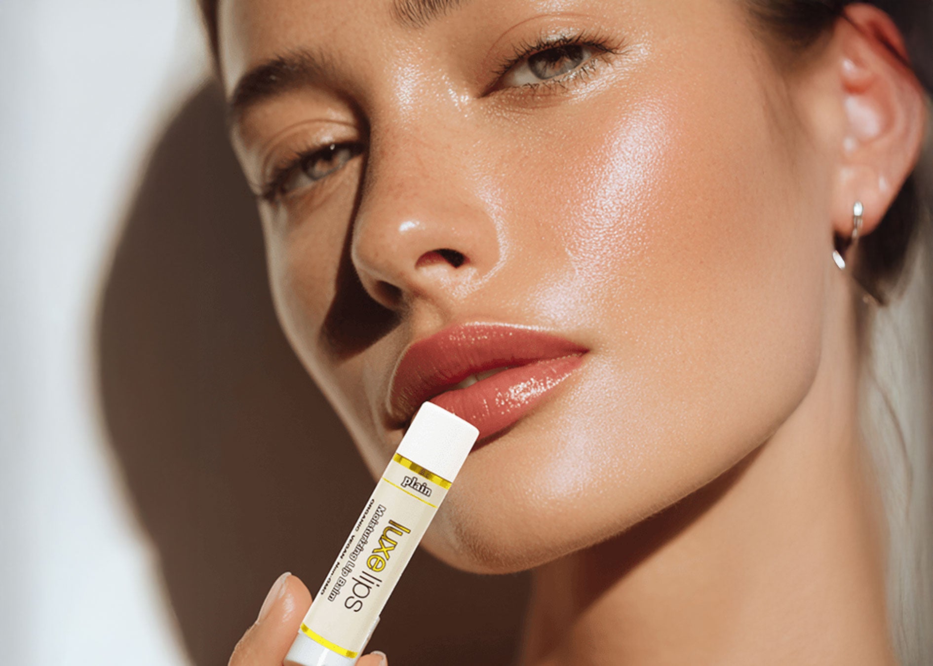 Close-up of a woman holding a Luxe Lips lip balm with a blurred background